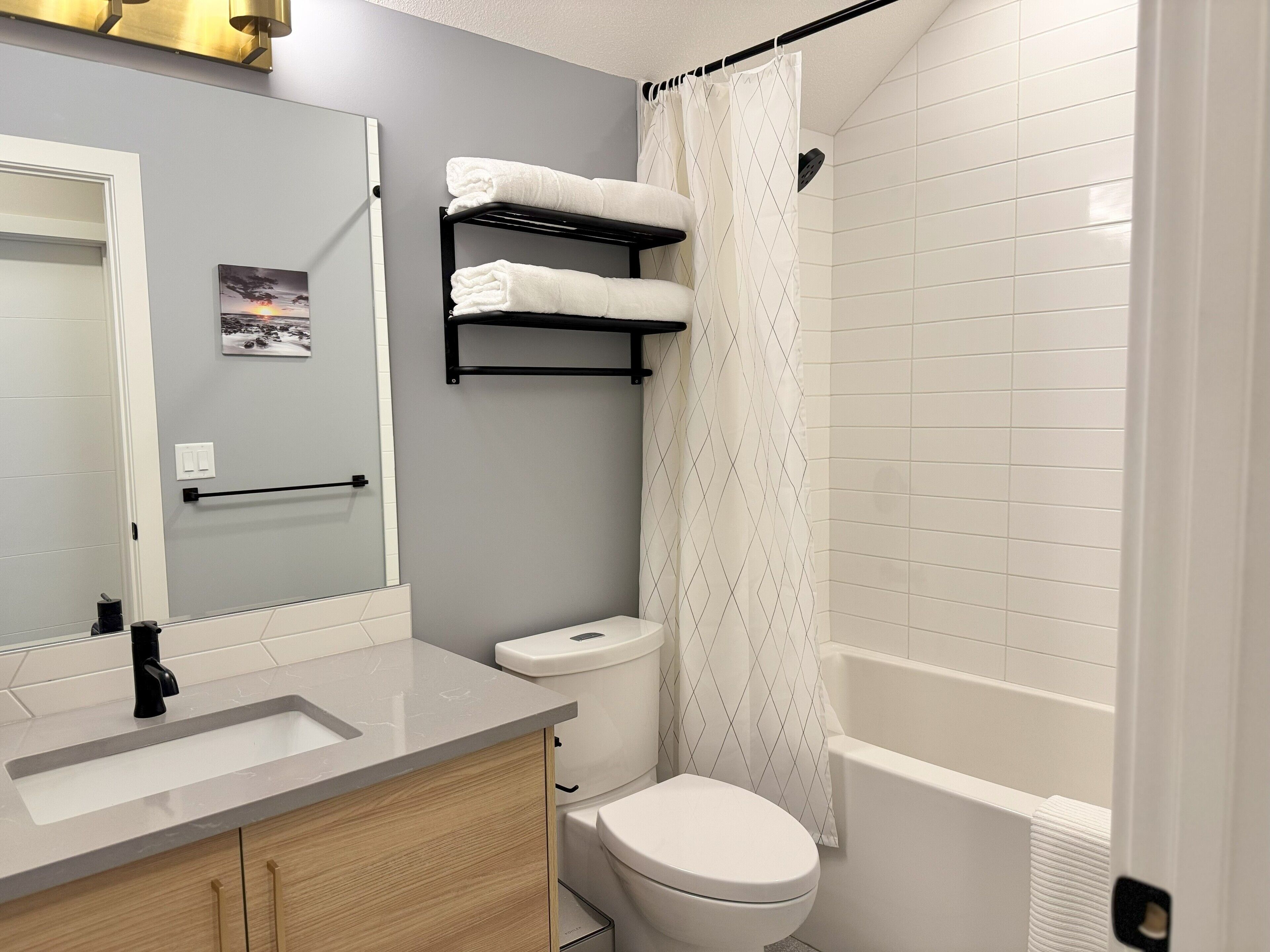 A bathroom with a white sink, a toilet, a shower with a curtain, and a towel rack with towels.