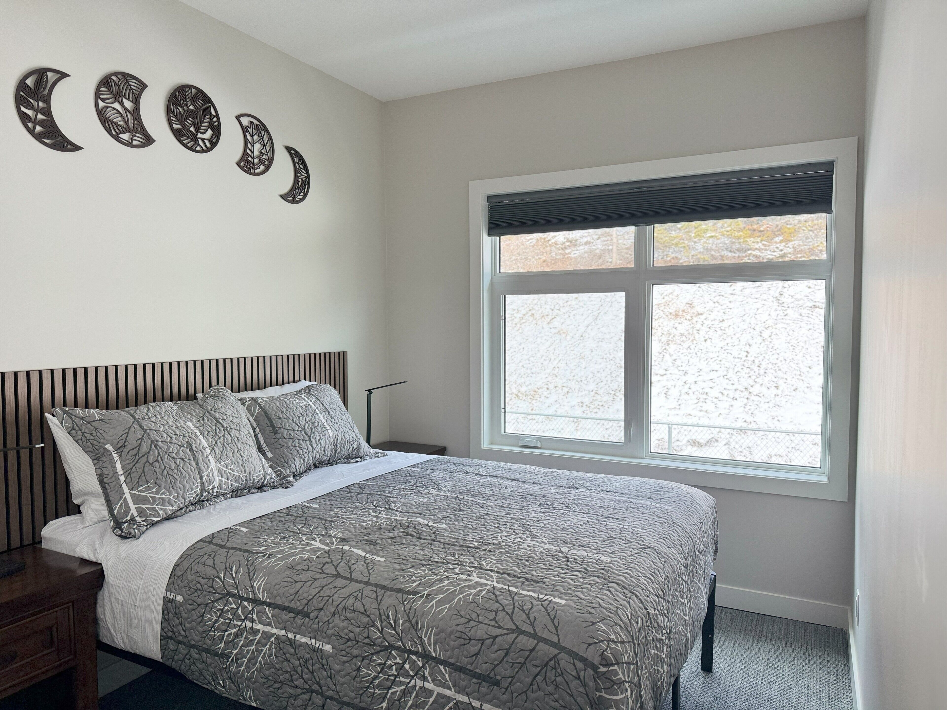 A bedroom with a bed, a nightstand, a window with blinds, and wall art.