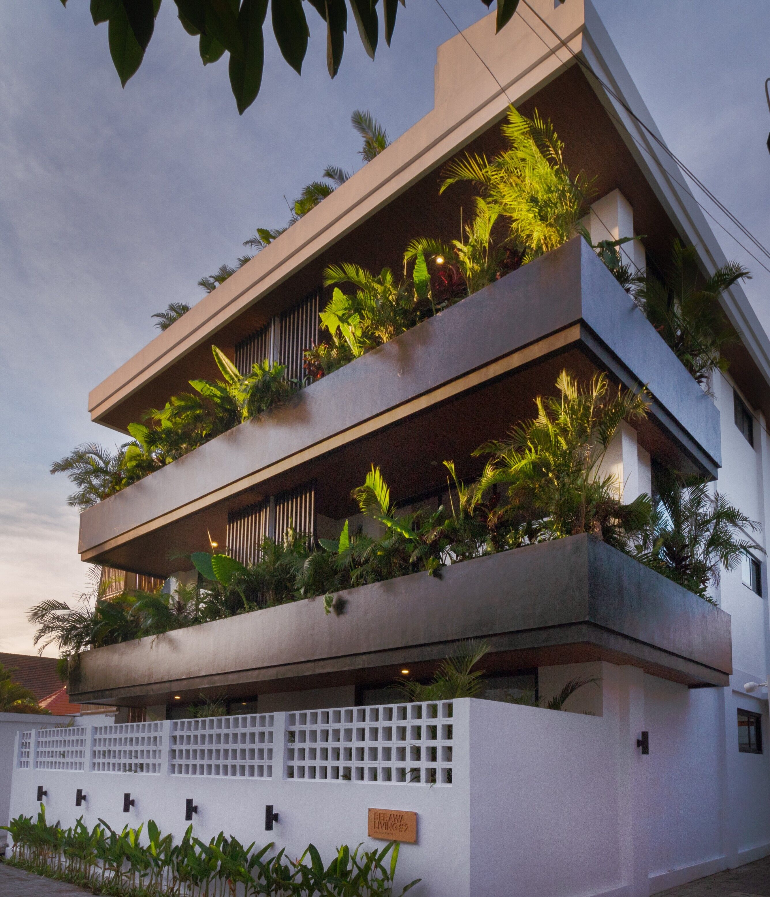A modern multi-story building with balconies, some of which are covered with plants.