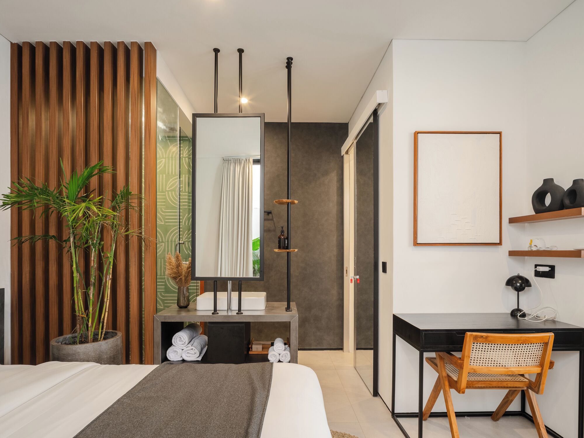A modern bedroom with a bed, a desk, a chair, a large mirror, and a potted plant.
