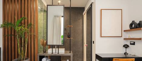 A modern bedroom with a bed, a desk, a chair, a large mirror, and a potted plant.
