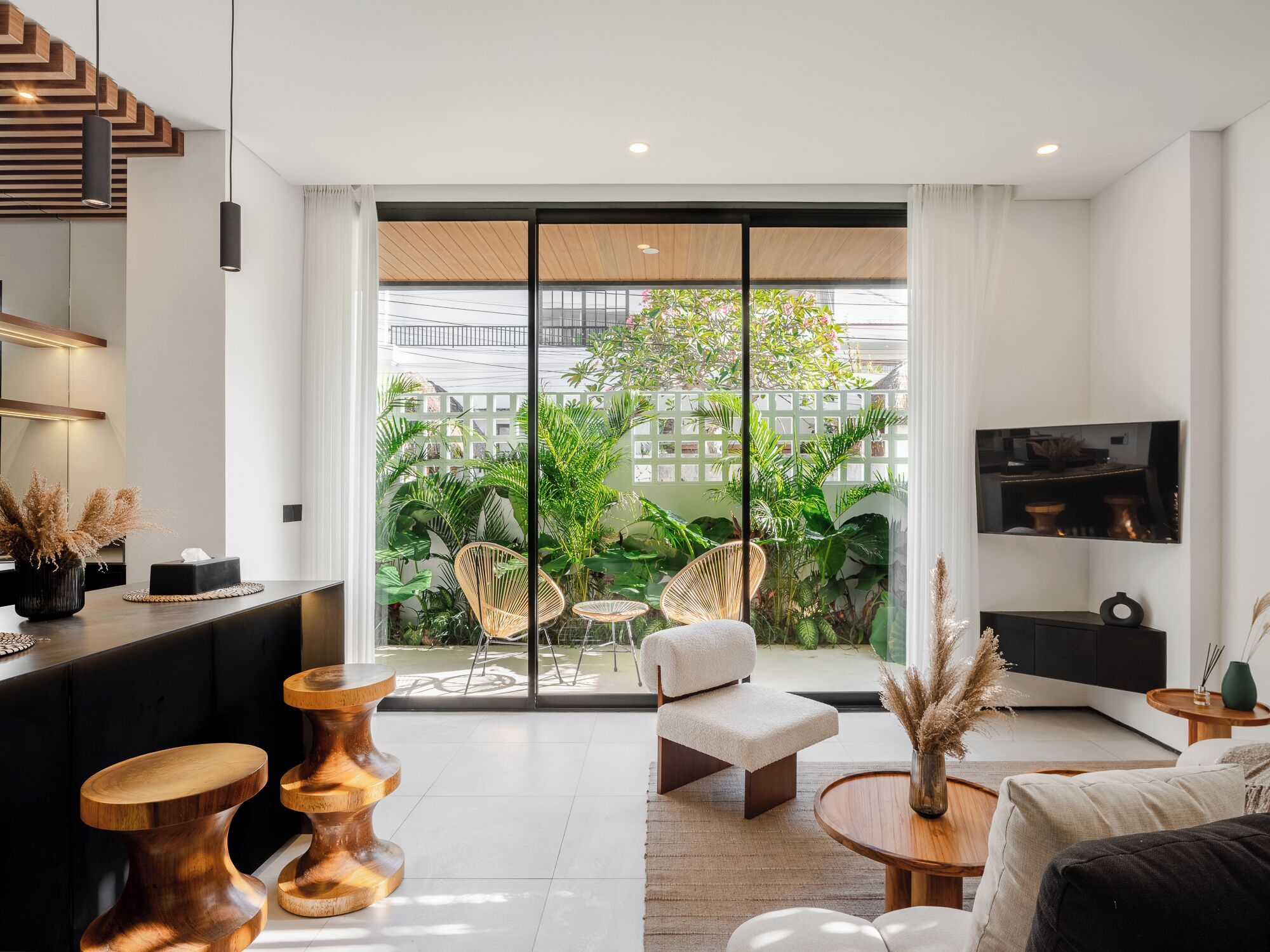Un salon moderne doté d’une grande porte-fenêtre coulissante qui donne sur un balcon agrémenté d’une végétation luxuriante.