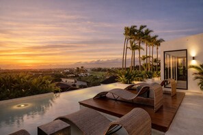A rooftop infinity pool with lounge chairs, palm trees, and a sunset view.