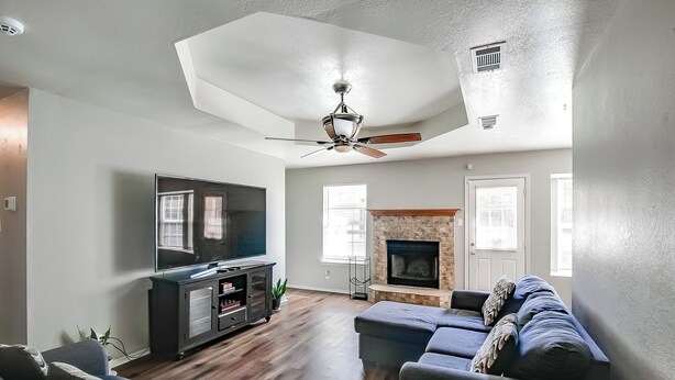 A living room with a flat-screen TV, dark-colored sofas, a fireplace, and a ceiling fan.