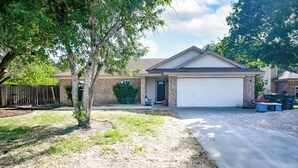A residential house with a garage, a driveway, and a tree in the front yard.
