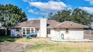 A single-story house with a chimney, a front porch, and a backyard with a grill and chairs.