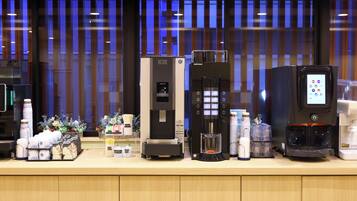 A row of beverage dispensers, including an ICE machine and a coffee maker, with various cups and containers on a counter.