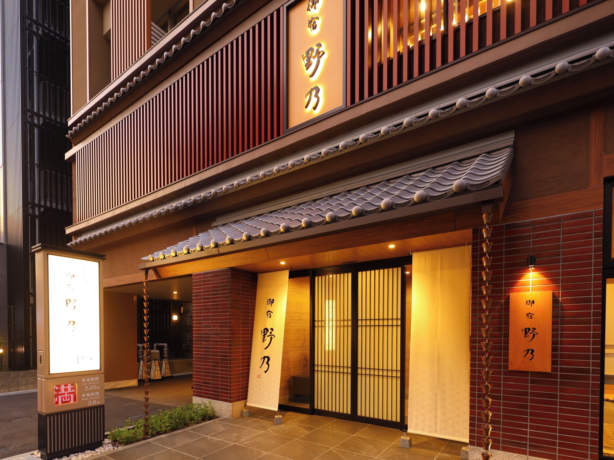 A traditional Japanese building with a signboard, a tiled entrance, and a wooden fence.