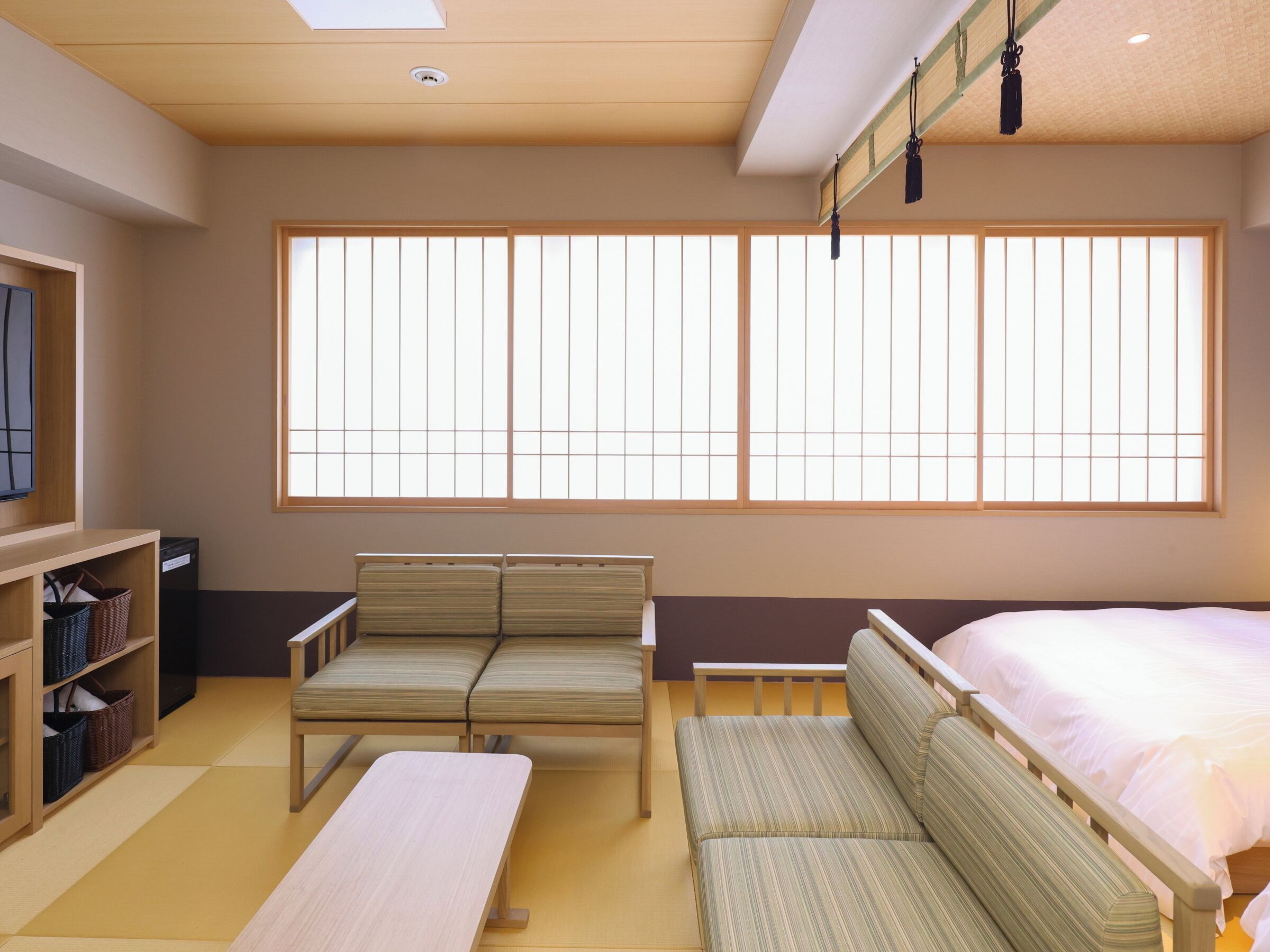 A room with a bed, two seating areas, a TV, and a window with vertical blinds.