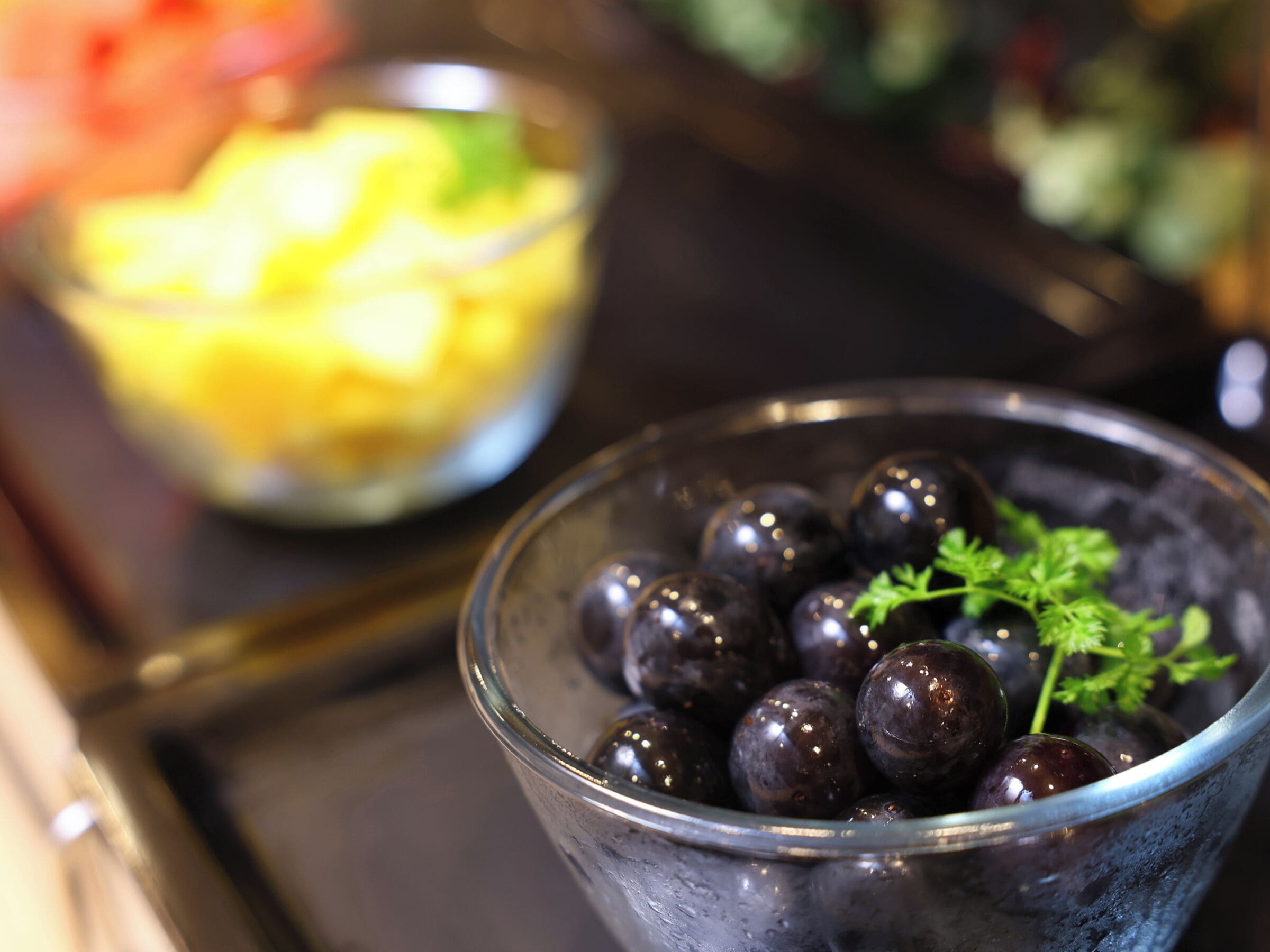 A glass bowl filled with dark-colored grapes and a sprig of parsley, placed on a tray.