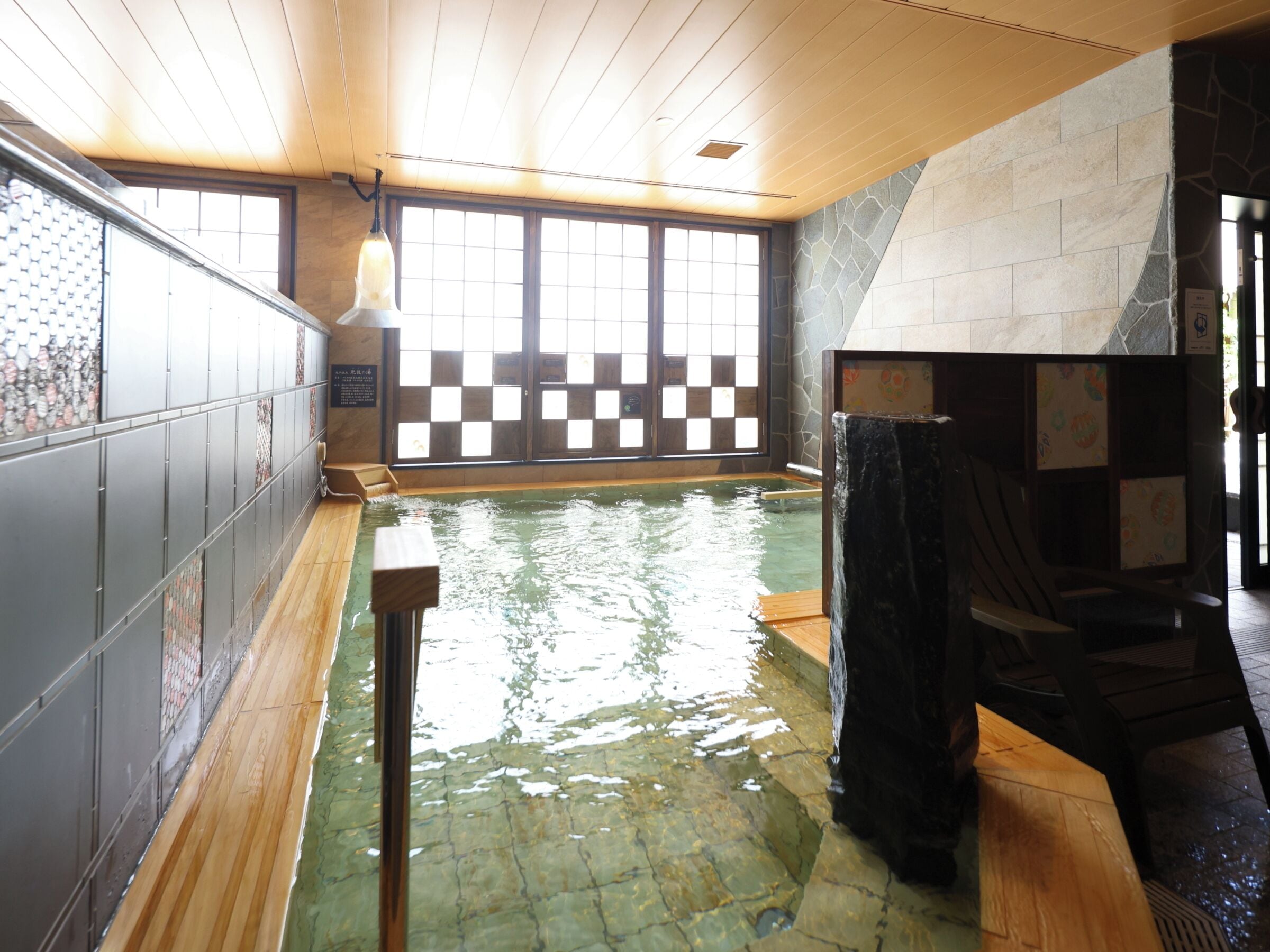 Un onsen japonais traditionnel, avec un plancher en bois, des murs en pierre et une vue sur l’extérieur grâce à de grandes fenêtres.