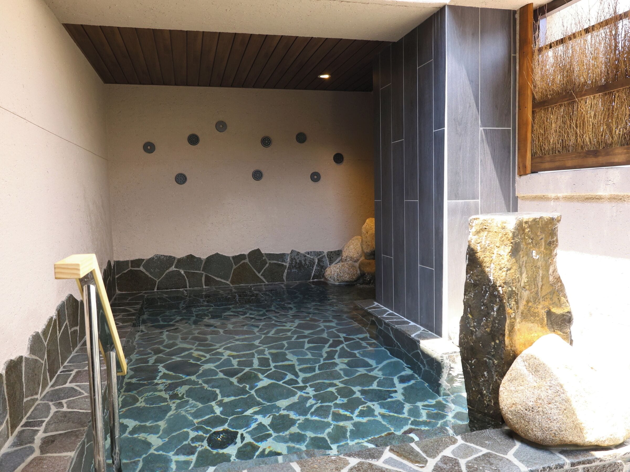 Un jacuzzi con suelo de mosaico de piedra, rodeado de paredes de piedra y techo de madera.