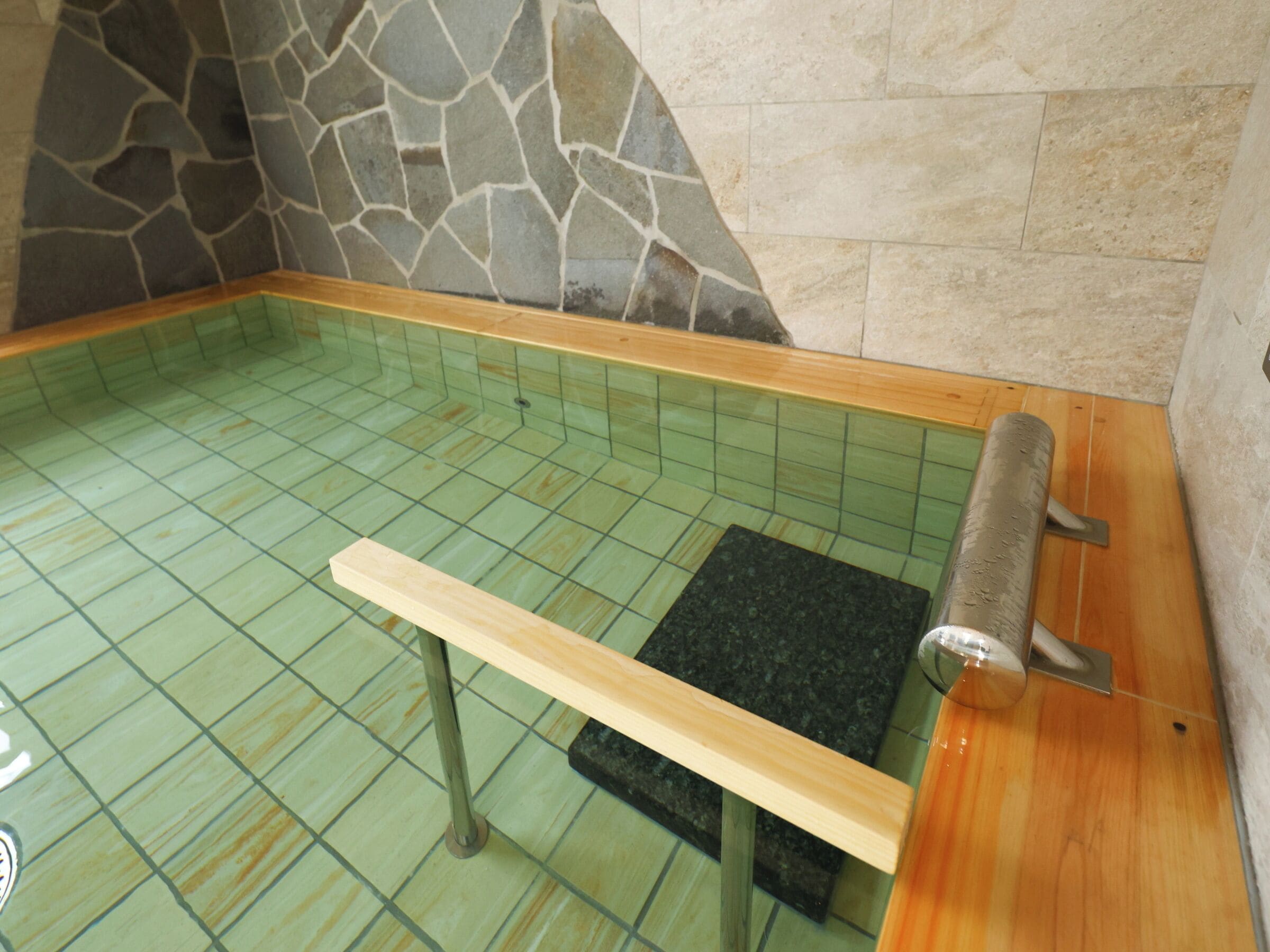 Uma área de spa com parede de pedra, chão em azulejo, banco de madeira e mesa de massagem.