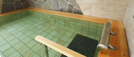 Uma área de spa com parede de pedra, chão em azulejo, banco de madeira e mesa de massagem.