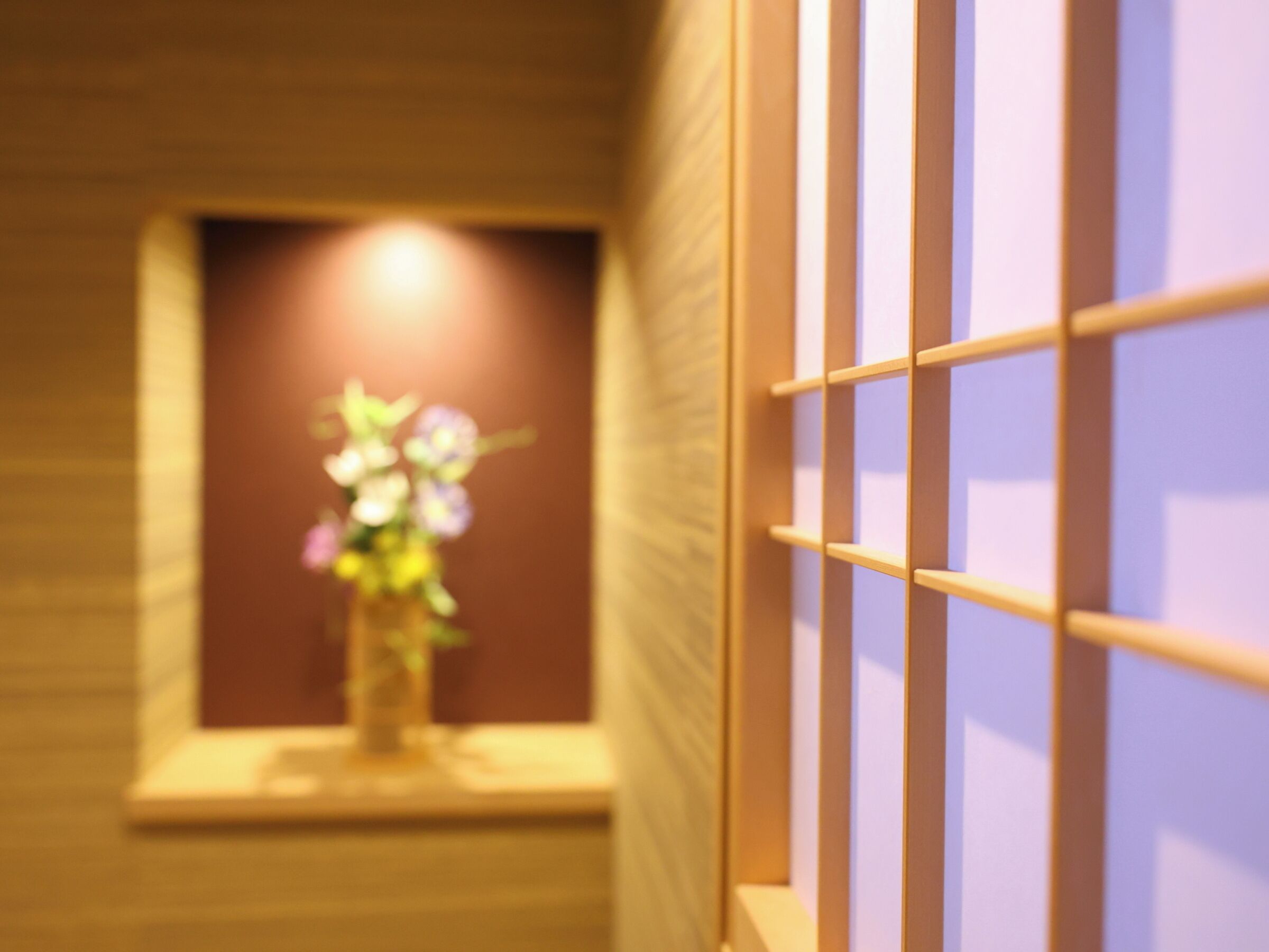 A corridor with a wooden floor and a window with a vase of flowers.