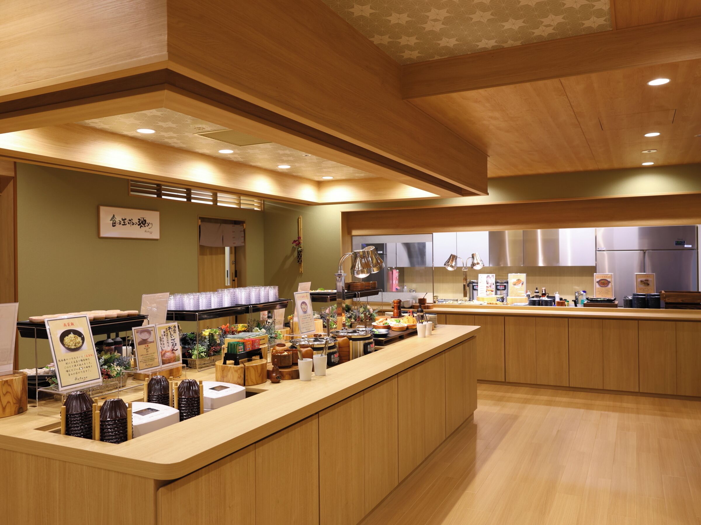 A modern restaurant interior with wooden paneling, a central counter with food displays, and a clean, organized layout.