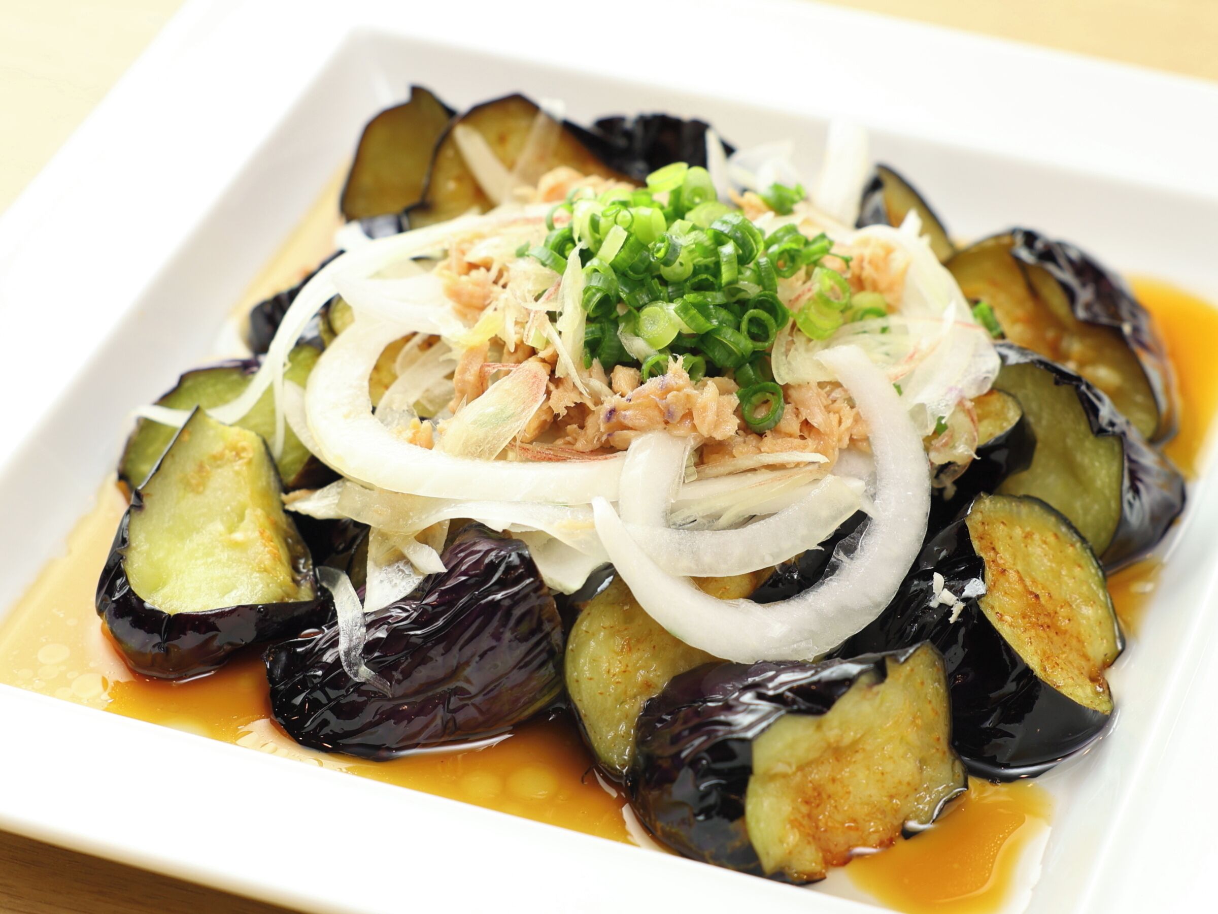 Un piatto con fette di melanzane, cipolle e cipollotti in una ciotola bianca.
