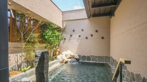 A spa area with a stone pool, a wooden deck, and a stone wall with a water feature. - Natural Hot Spring Higo no Yu Onyado Nono Kumamoto (Kumamoto)