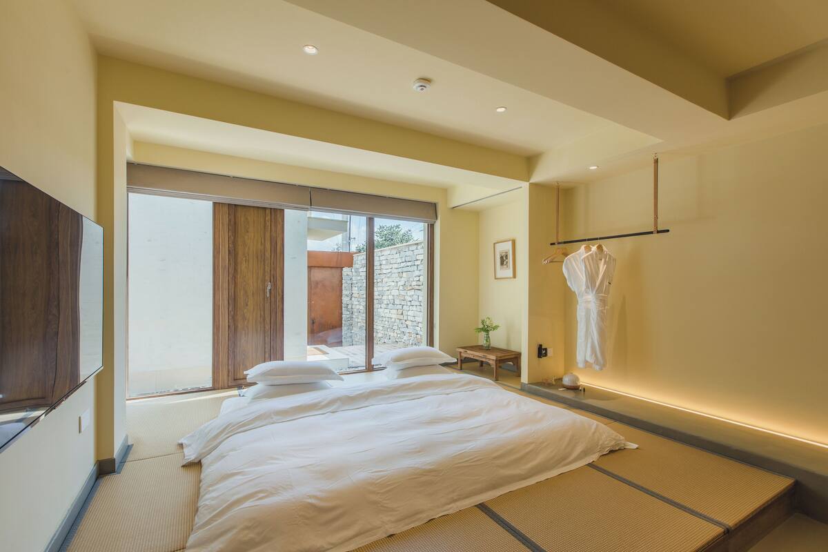 A modern bedroom with a large bed, a sliding glass door leading to a balcony, and a wall-mounted TV.