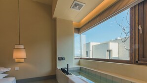 Un baño moderno con bañera, toallero y ventana que ofrece vistas de edificios.