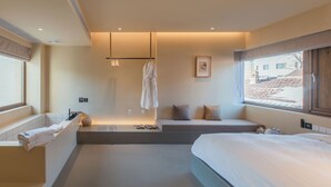 Un baño de hotel moderno con bañera, un ventanal grande y una zona de estar con cojines.