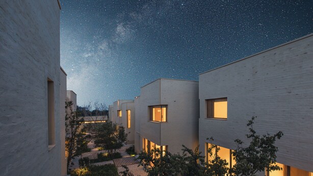 Un complejo moderno de edificios con varias unidades, cada una con grandes ventanales y un patio interior.