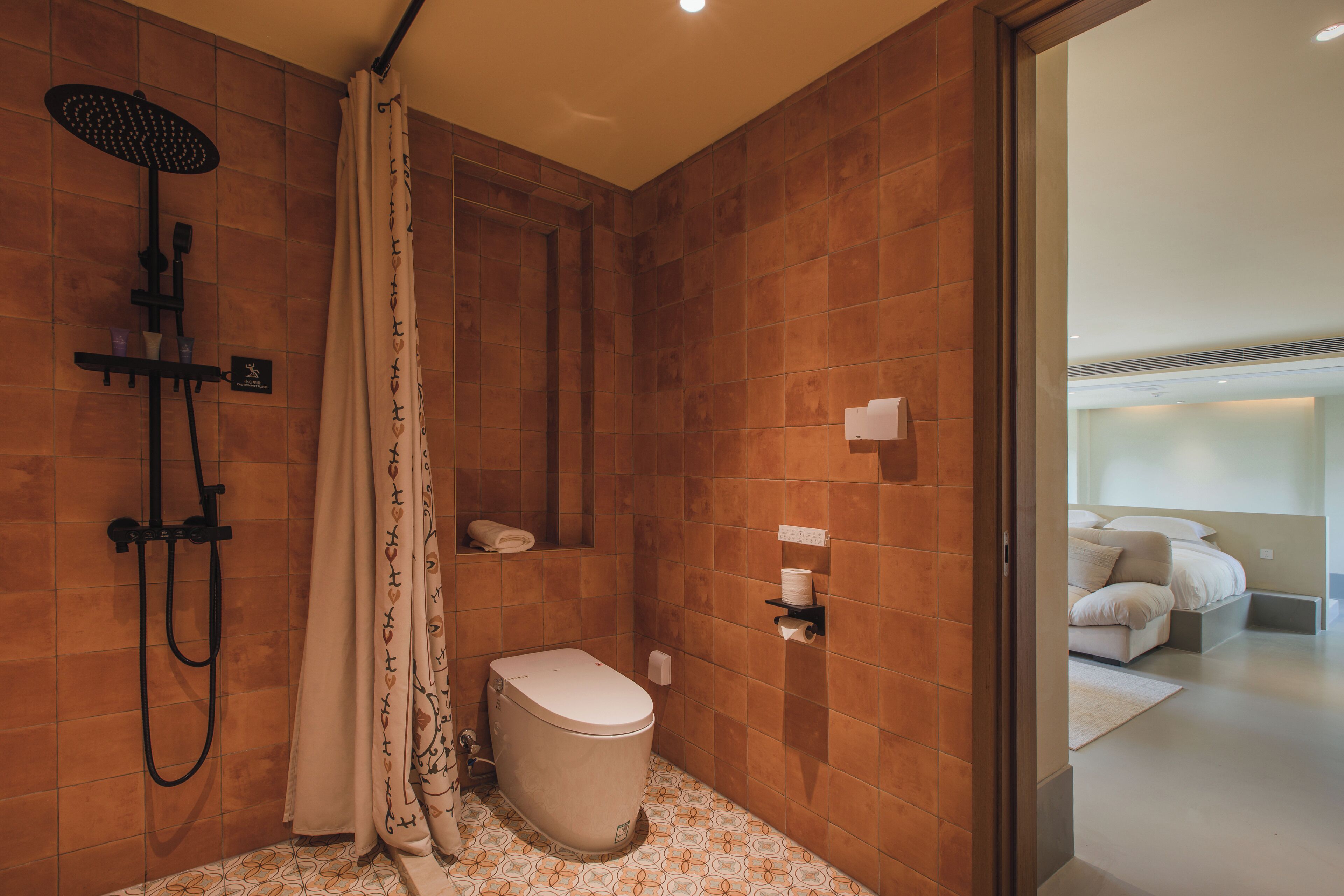 A modern bathroom with a shower, toilet, and a small shelf with toiletries.
