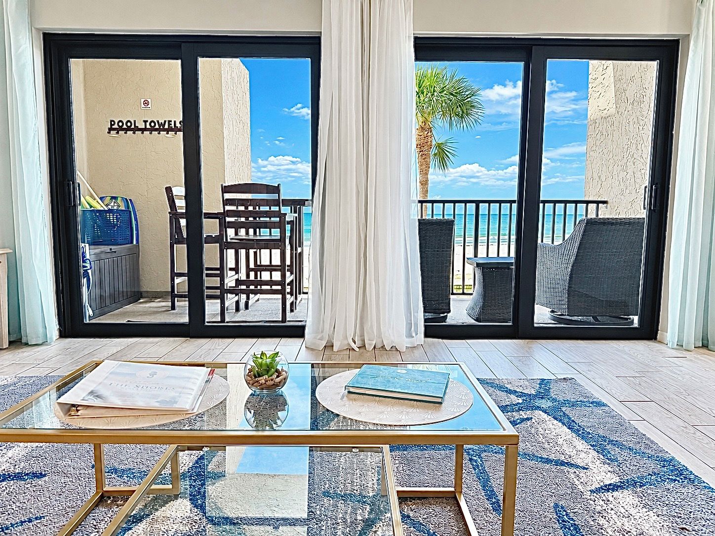 A room with a glass table, a chair, a small plant, and a view of the beach through a sliding door.