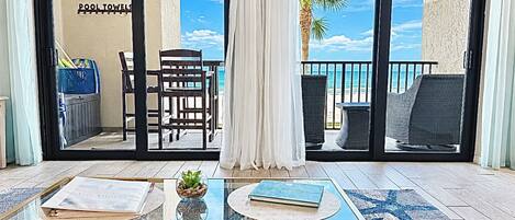 Ein Zimmer mit Glastisch, Stuhl, einer kleinen Pflanze und Blick auf den Strand durch eine Schiebetür.