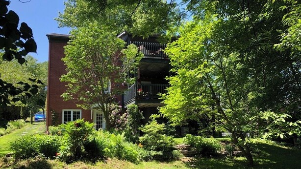 A two-story building with a balcony, surrounded by lush greenery and a well-maintained lawn. - Le Havre Gris, a spacious private room for relaxing or working (Sherbrooke)