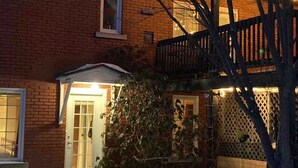 A brick house with a front porch, a wooden deck, and a snow-covered ground. - Le Havre Gris, a spacious private room for relaxing or working (Sherbrooke)