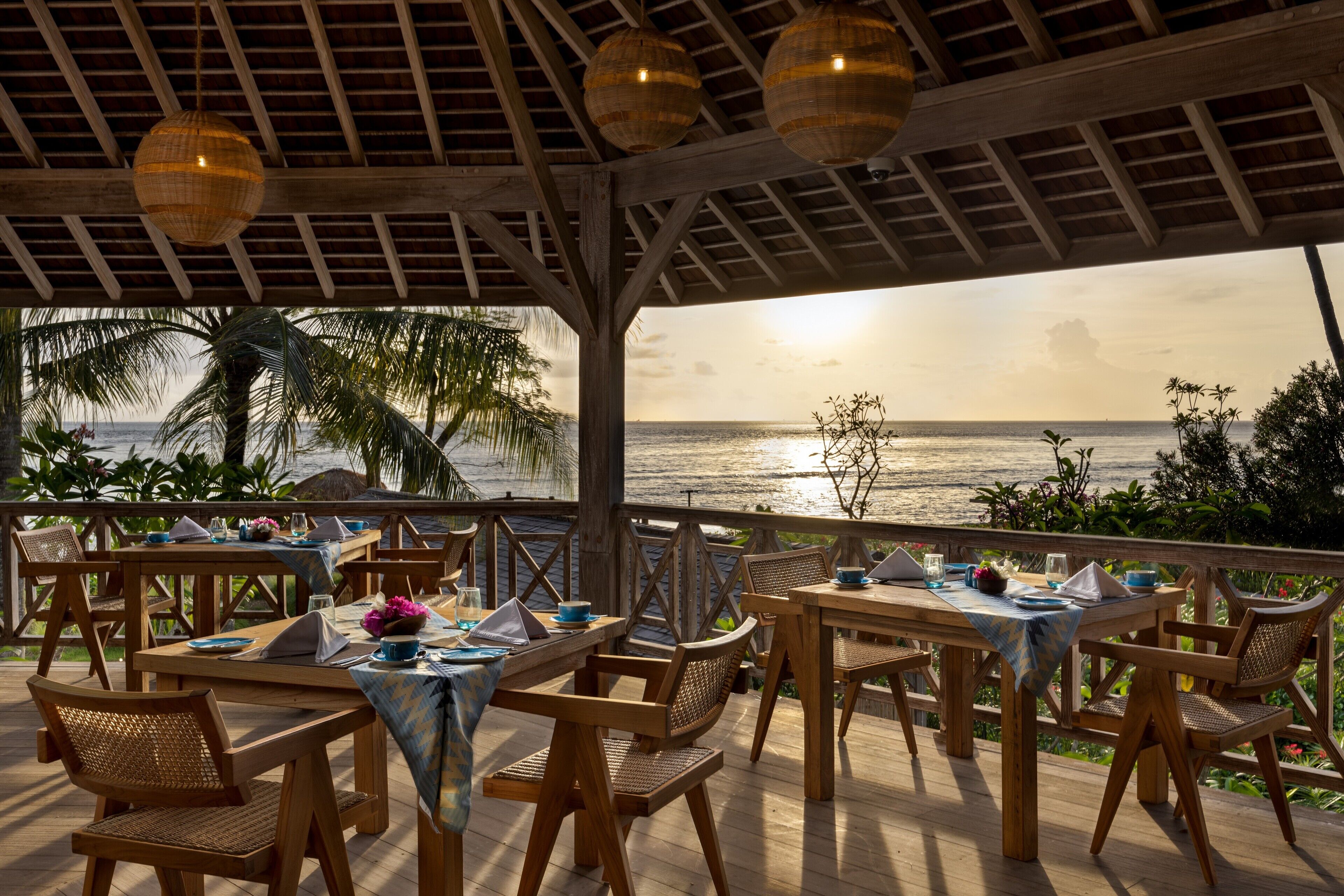 An outdoor dining area with wooden tables and chairs, overlooking a beach.
