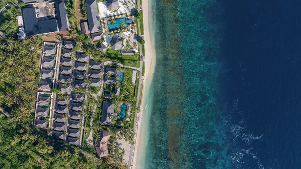 An aerial view of a resort with multiple buildings, a beach, and clear turquoise waters.