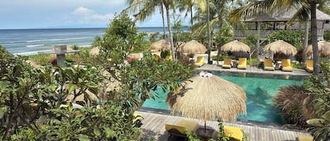 A resort pool area with thatched umbrellas, lounge chairs, and a view of the ocean.