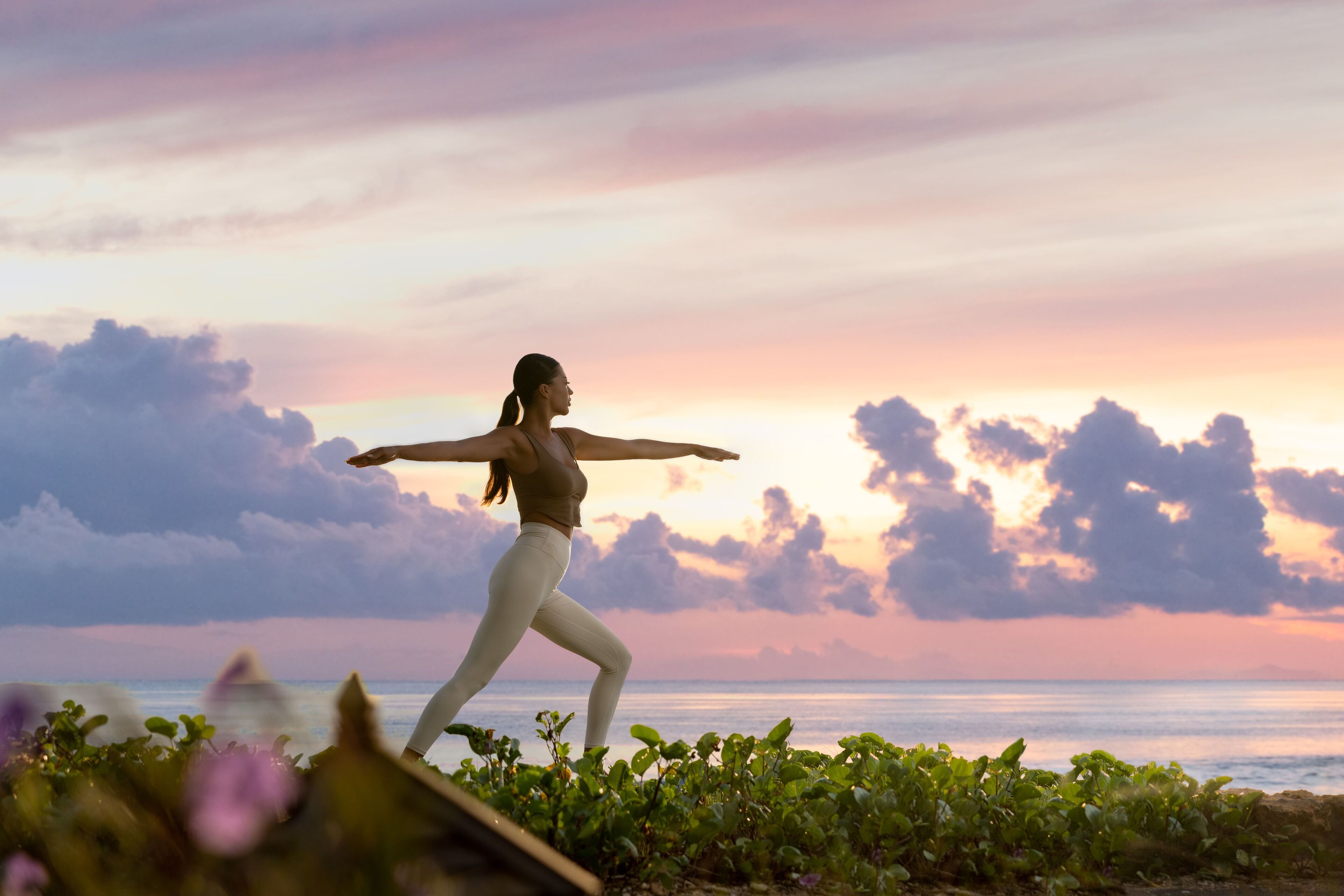 Une personne effectuant une posture de yoga sur une plage, avec un coucher de soleil en arrière-plan.
