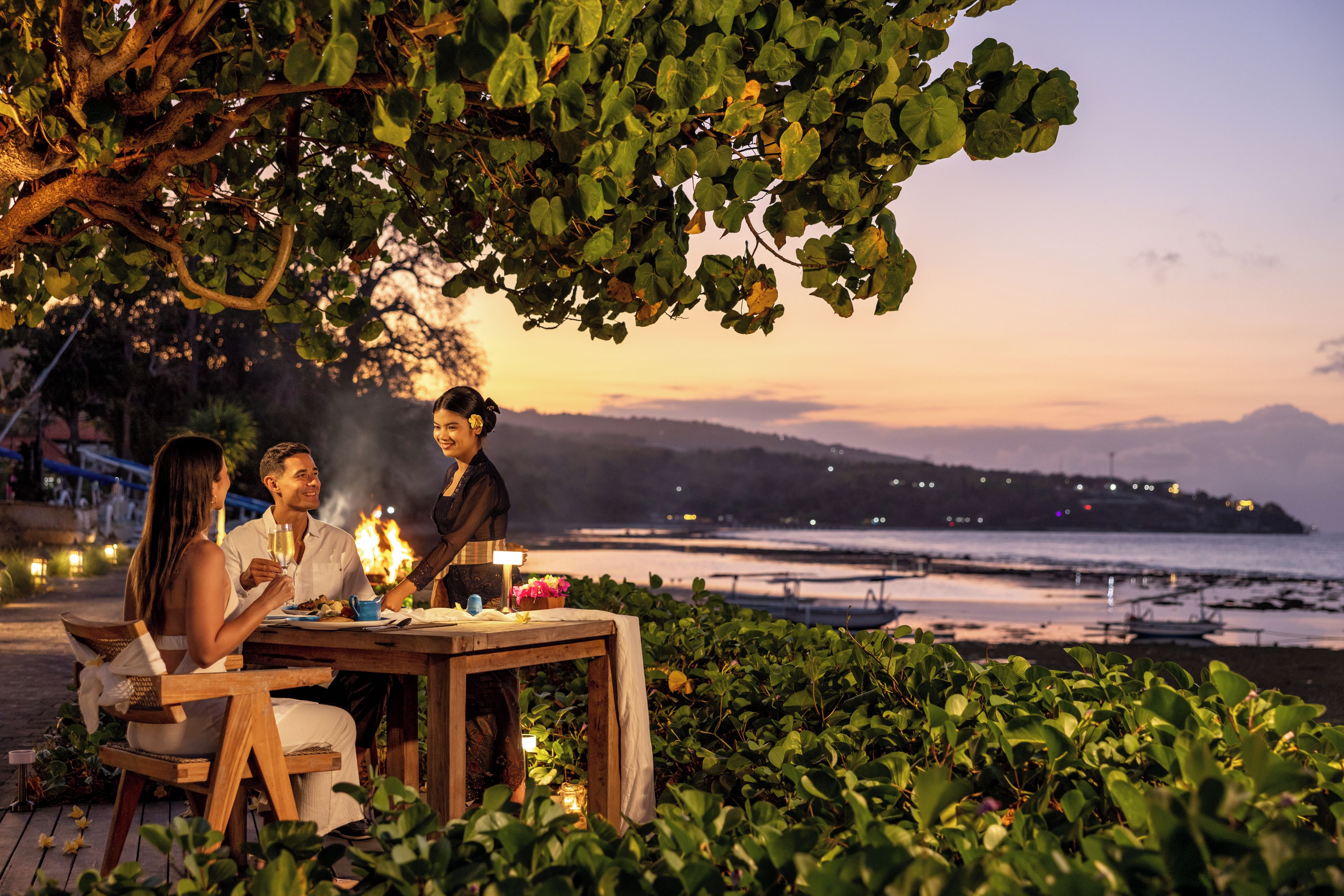 A dining table set outdoors with a view of the sea and mountains in the background.