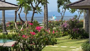 A tropical garden with a pool, palm trees, and a view of the ocean.
