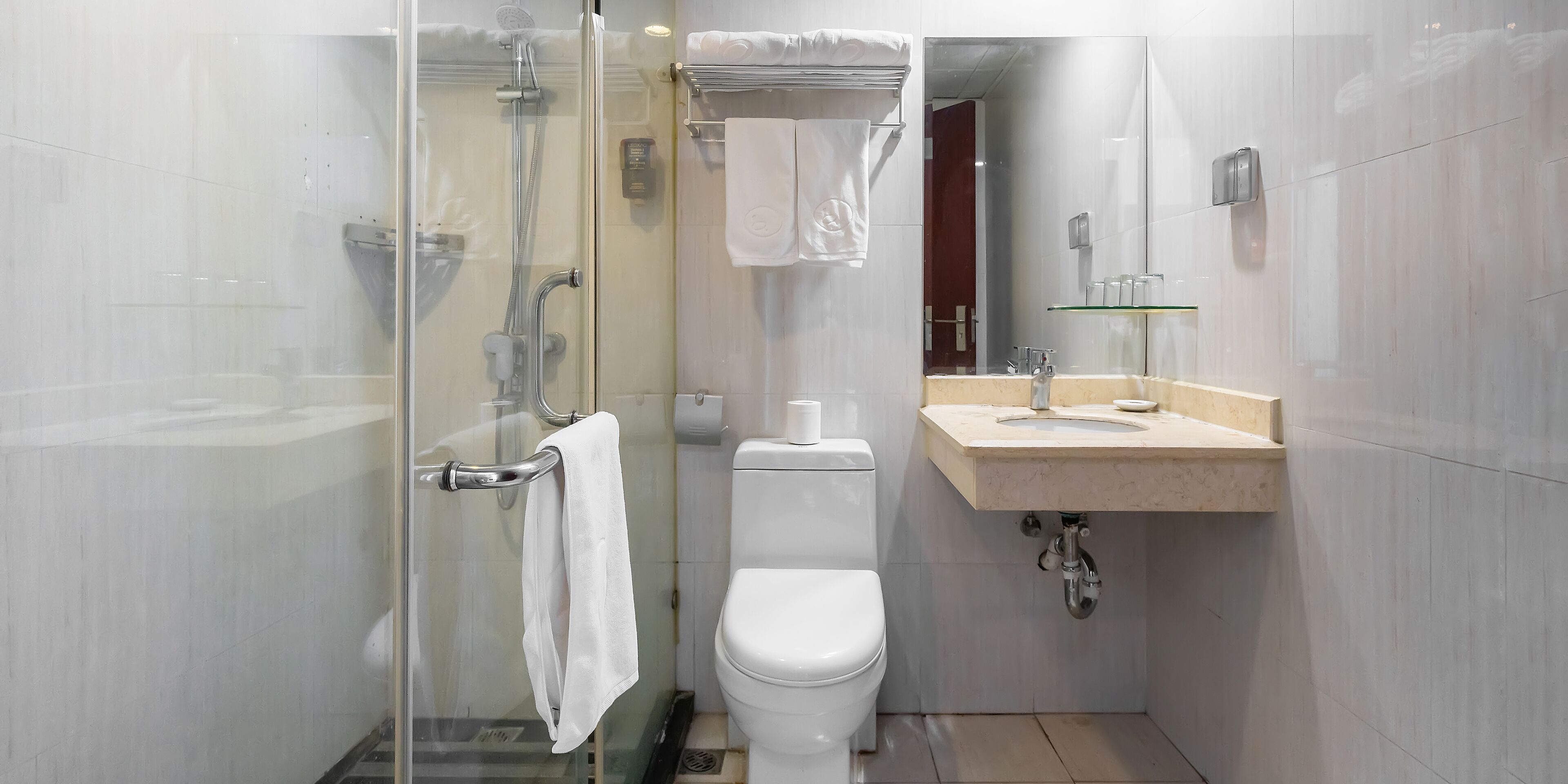 Een moderne badkamer met een douche met glazen wand, een wit toilet en een beige wastafelmeubel met spiegel.