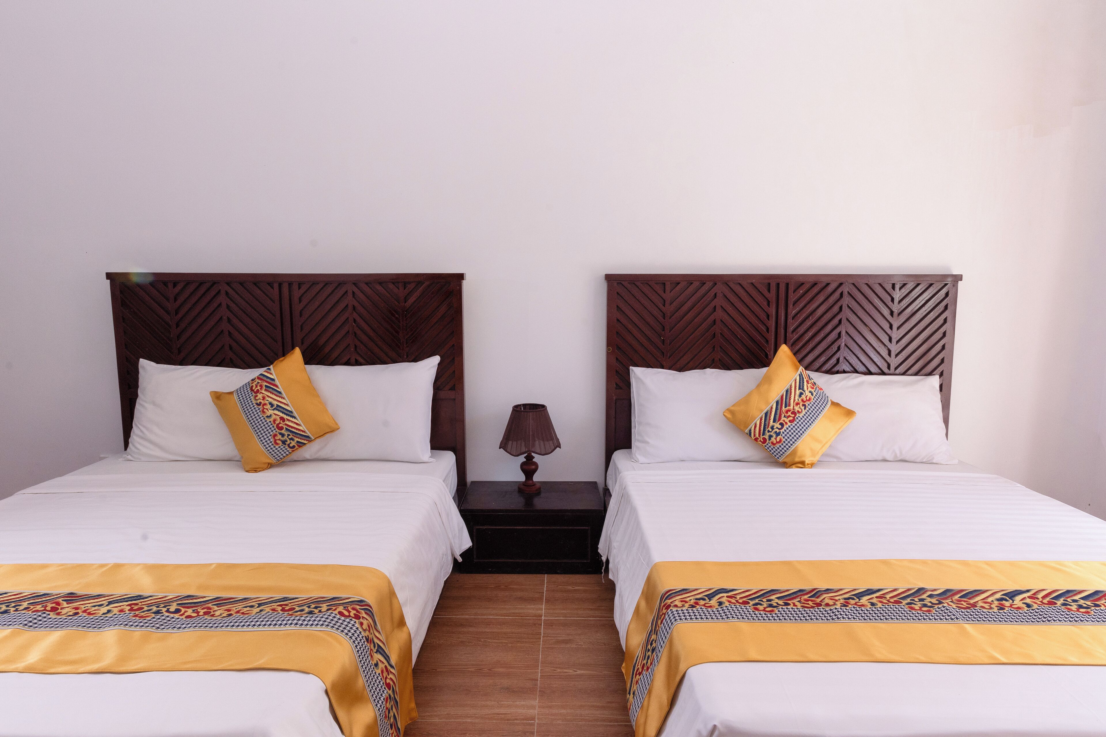 A hotel room with two beds, each with a wooden headboard, white bedding, and a patterned yellow throw blanket.