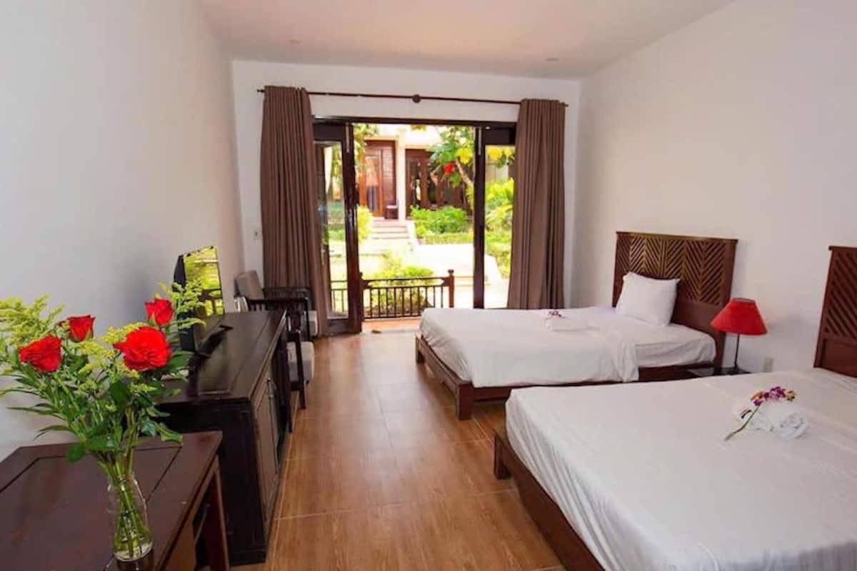 A hotel room with two beds, a desk, and a view of the garden.