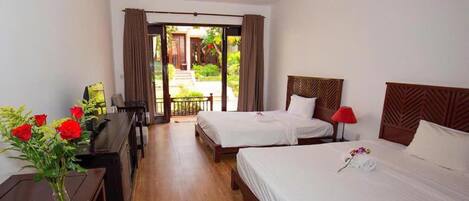 A hotel room with two beds, a desk, and a view of the garden.