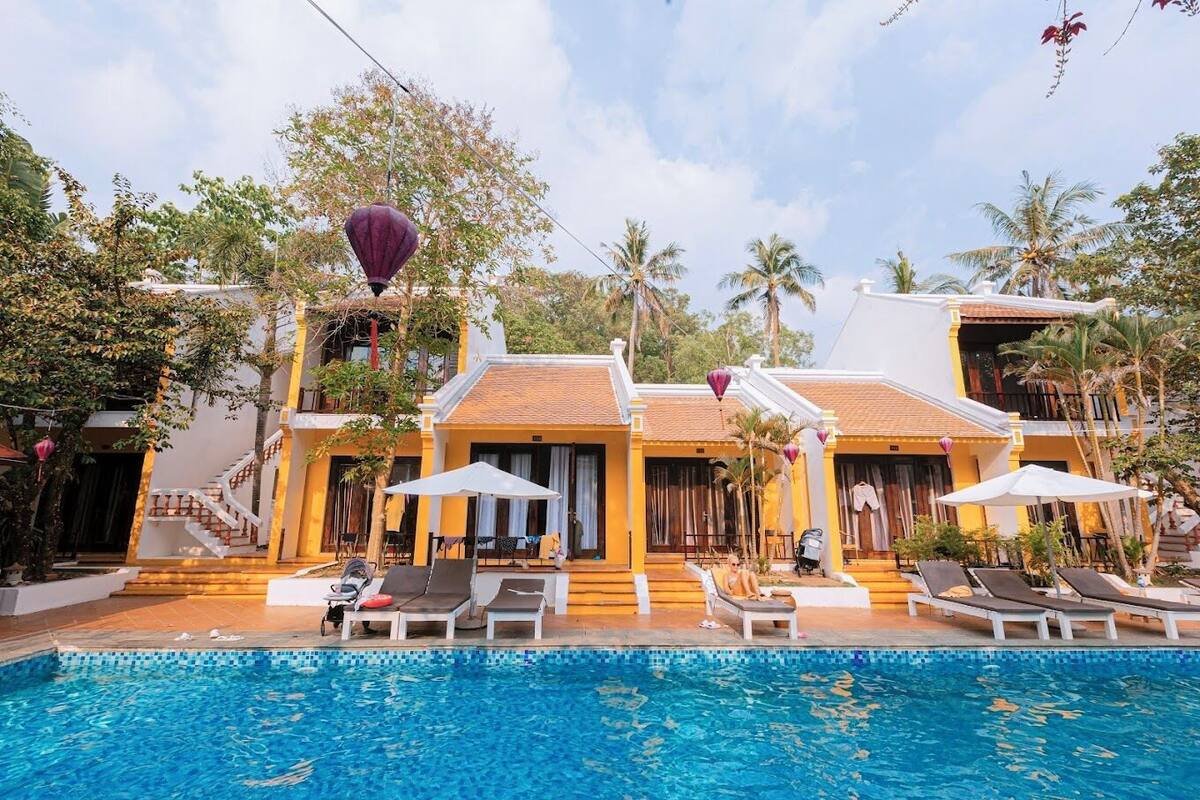 A hotel with a swimming pool, lounge chairs, and a staircase leading to the entrance.
