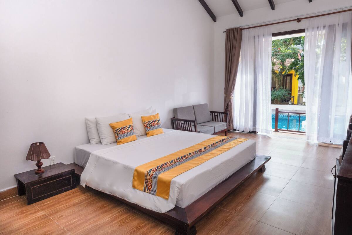 A bedroom with a large bed, a nightstand, a chair, and a view of a pool.