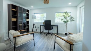 A modern office space with a desk, office chair, bookshelf, two sofas, and a potted plant.