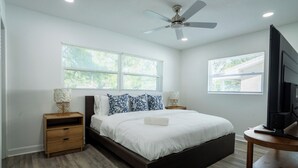 A bedroom with a bed, two bedside tables, a ceiling fan, and a TV.