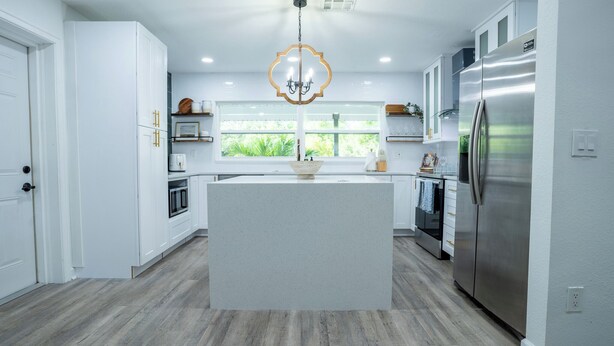 A modern kitchen with white cabinetry, a central island, stainless steel appliances, and a view through the window.