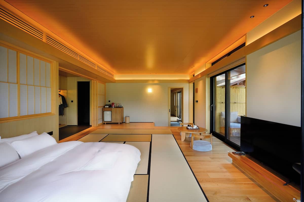 Una habitación de hotel con una cama, televisión, una mesita pequeña y una puerta corredera que da a un balcón.