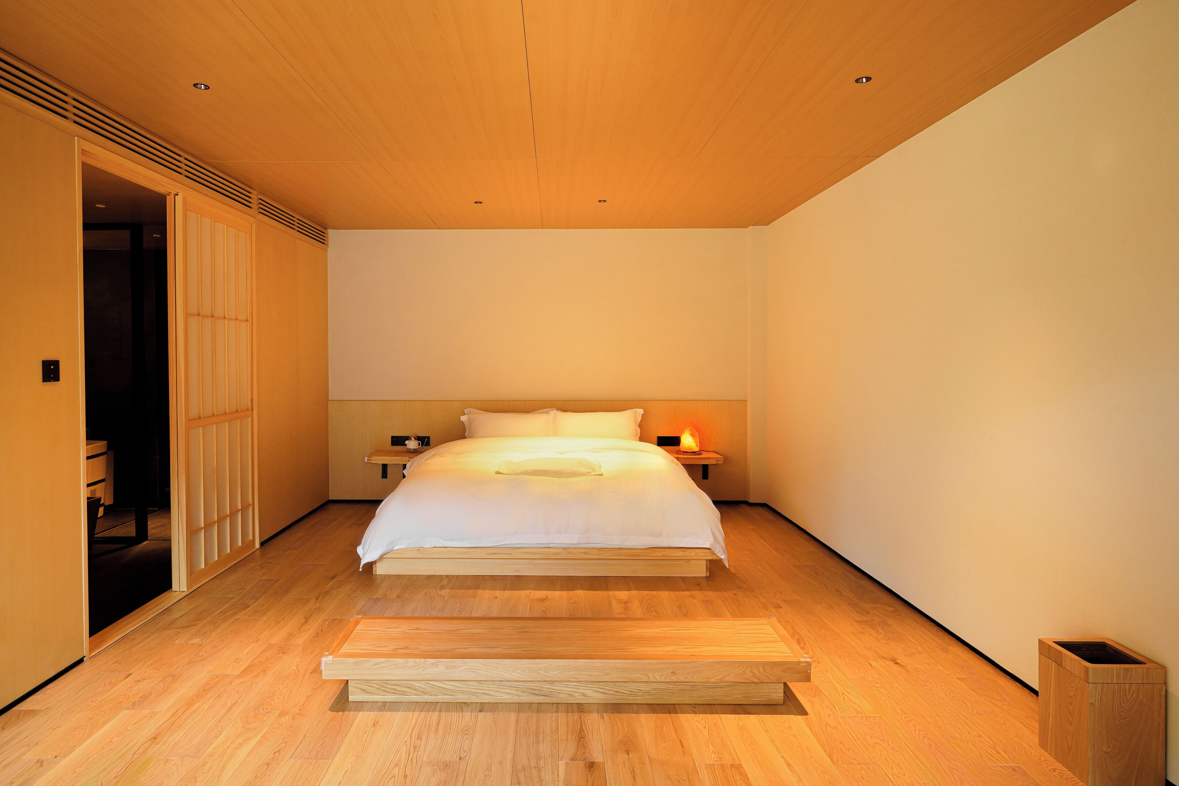 A minimalist bedroom with a wooden bed, a nightstand, and a bedside table with a lamp.