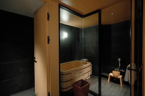 Een moderne badkamer met een douchecabine van glas, een houten bad en een klein houten krukje.
