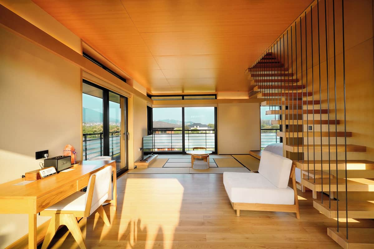 Un interior moderno con escritorio de madera, sofá blanco, esteras de tatami y una escalera.